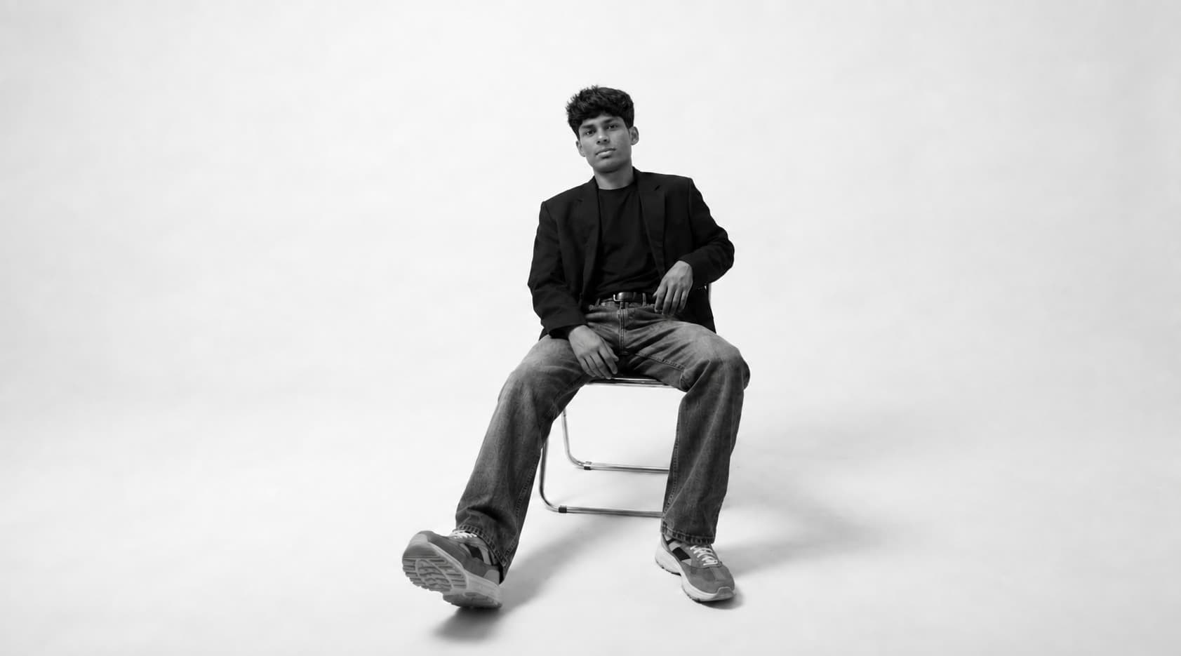 Krishna Mundra seated on a chair in a black blazer, monochrome studio portrait